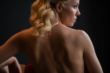 Adult beauty woman bare back in formal evening red trousers sitting pose without bra. Stylish blonde curly hair sensual nude model fashionista posing at studio in fashion pantsuit out of blazer