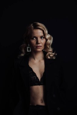 Young adult beauty woman in formal evening suit of black color with lace bra at thoughtful. Stylish blonde curly hair sensual model fashionista posing at studio in fashion pantsuit