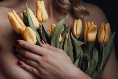 Yetişkin, güzel bir kadın, yarı çıplak, resmi kırmızı pantolonlu, sütyensiz, sarı laleli. Şık, kıvırcık saçlı, seksi, çıplak model model, bahar tatilinde stüdyoda poz veriyor.