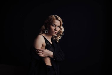 Young adult beauty woman in formal evening suit of black color with lace bra at thoughtful. Stylish blonde curly hair sensual model fashionista posing at studio in fashion pantsuit