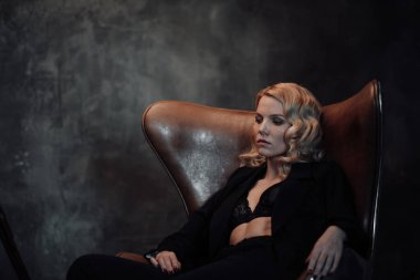 Young adult beauty woman in formal evening suit of black color with lace bra at thoughtful. Stylish blonde curly hair sensual model fashionista posing at studio in fashion pantsuit