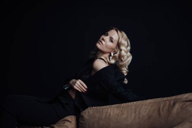 Young adult beauty woman in formal evening suit of black color with lace bra at thoughtful. Stylish blonde curly hair sensual model fashionista posing at studio in fashion pantsuit