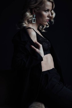 Young adult beauty woman in formal evening suit of black color with lace bra at thoughtful. Stylish blonde curly hair sensual model fashionista posing at studio in fashion pantsuit