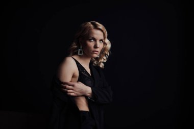 Young adult beauty woman in formal evening suit of black color with lace bra at thoughtful. Stylish blonde curly hair sensual model fashionista posing at studio in fashion pantsuit