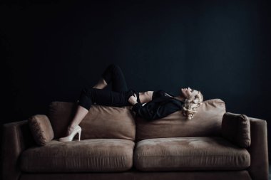 Young adult beauty woman in formal evening suit of black color with lace bra at thoughtful. Stylish blonde curly hair sensual model fashionista posing at studio in fashion pantsuit