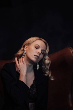 Young adult beauty woman in formal evening suit of black color with lace bra at thoughtful. Stylish blonde curly hair sensual model fashionista posing at studio in fashion pantsuit