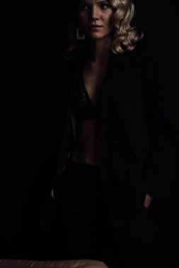 Young adult beauty woman in formal evening suit of black color with lace bra at thoughtful. Stylish blonde curly hair sensual model fashionista posing at studio in fashion pantsuit