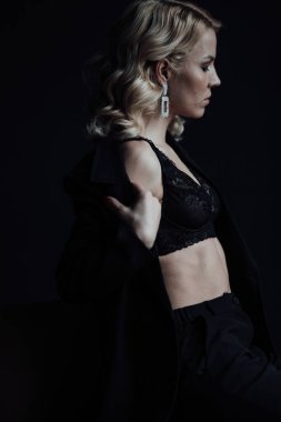Young adult beauty woman in formal evening suit of black color with lace bra at thoughtful. Stylish blonde curly hair sensual model fashionista posing at studio in fashion pantsuit