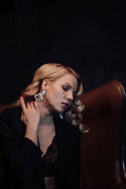 Young adult beauty woman in formal evening suit of black color with lace bra at thoughtful. Stylish blonde curly hair sensual model fashionista posing at studio in fashion pantsuit