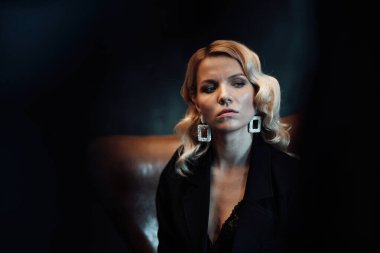 Young adult beauty woman in formal evening suit of black color with lace bra at thoughtful. Stylish blonde curly hair sensual model fashionista posing at studio in fashion pantsuit