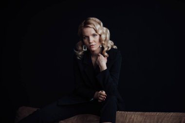 Young adult beauty woman in formal evening suit of black color with lace bra at thoughtful. Stylish blonde curly hair sensual model fashionista posing at studio in fashion pantsuit