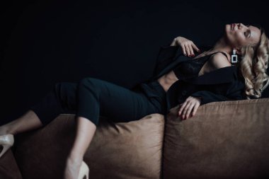 Young adult beauty woman in formal evening suit of black color with lace bra at thoughtful. Stylish blonde curly hair sensual model fashionista posing at studio in fashion pantsuit
