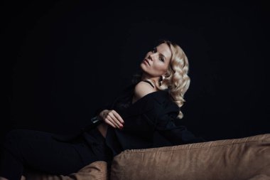 Young adult beauty woman in formal evening suit of black color with lace bra at thoughtful. Stylish blonde curly hair sensual model fashionista posing at studio in fashion pantsuit