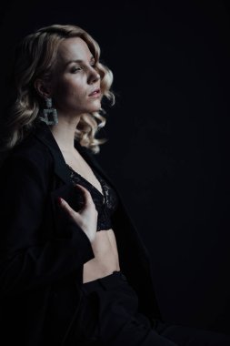 Young adult beauty woman in formal evening suit of black color with lace bra at thoughtful. Stylish blonde curly hair sensual model fashionista posing at studio in fashion pantsuit