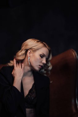 Young adult beauty woman in formal evening suit of black color with lace bra at thoughtful. Stylish blonde curly hair sensual model fashionista posing at studio in fashion pantsuit