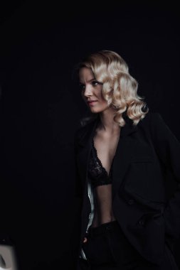 Young adult beauty woman in formal evening suit of black color with lace bra at thoughtful. Stylish blonde curly hair sensual model fashionista posing at studio in fashion pantsuit