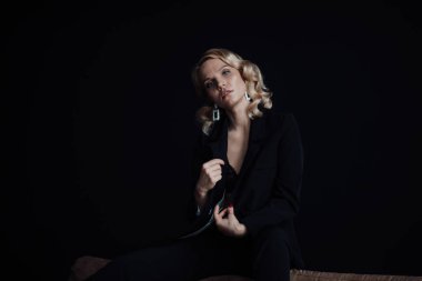 Young adult beauty woman in formal evening suit of black color with lace bra at thoughtful. Stylish blonde curly hair sensual model fashionista posing at studio in fashion pantsuit
