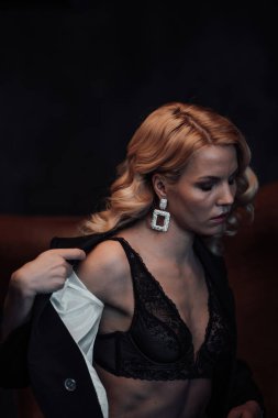 Young adult beauty woman in formal evening suit of black color with lace bra at thoughtful. Stylish blonde curly hair sensual model fashionista posing at studio in fashion pantsuit