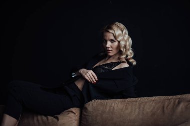 Young adult beauty woman in formal evening suit of black color with lace bra at thoughtful. Stylish blonde curly hair sensual model fashionista posing at studio in fashion pantsuit
