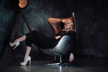 Young adult beauty woman in formal evening suit of black color with lace bra at thoughtful. Stylish blonde curly hair sensual model fashionista posing at studio in fashion pantsuit