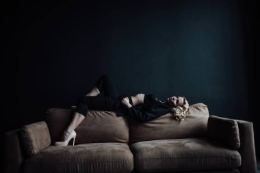 Young adult beauty woman in formal evening suit of black color with lace bra at thoughtful. Stylish blonde curly hair sensual model fashionista posing at studio in fashion pantsuit