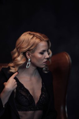 Young adult beauty woman in formal evening suit of black color with lace bra at thoughtful. Stylish blonde curly hair sensual model fashionista posing at studio in fashion pantsuit