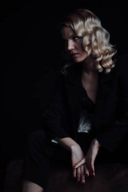 Young adult beauty woman in formal evening suit of black color with lace bra at thoughtful. Stylish blonde curly hair sensual model fashionista posing at studio in fashion pantsuit