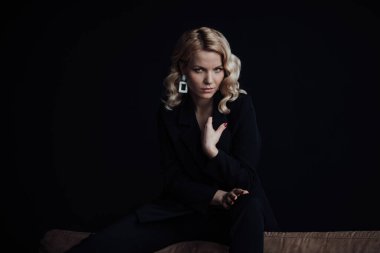 Young adult beauty woman in formal evening suit of black color with lace bra at thoughtful. Stylish blonde curly hair sensual model fashionista posing at studio in fashion pantsuit