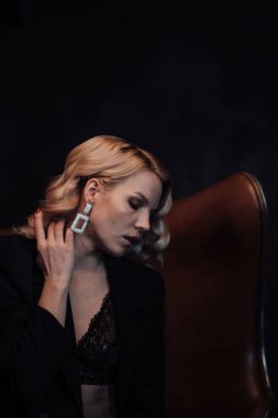 Young adult beauty woman in formal evening suit of black color with lace bra at thoughtful. Stylish blonde curly hair sensual model fashionista posing at studio in fashion pantsuit