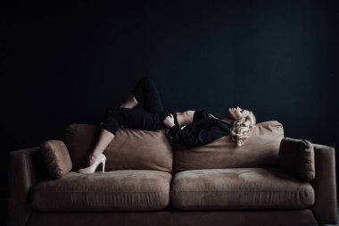 Young adult beauty woman in formal evening suit of black color with lace bra at thoughtful. Stylish blonde curly hair sensual model fashionista posing at studio in fashion pantsuit