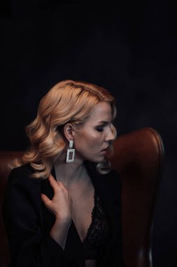 Young adult beauty woman in formal evening suit of black color with lace bra at thoughtful. Stylish blonde curly hair sensual model fashionista posing at studio in fashion pantsuit