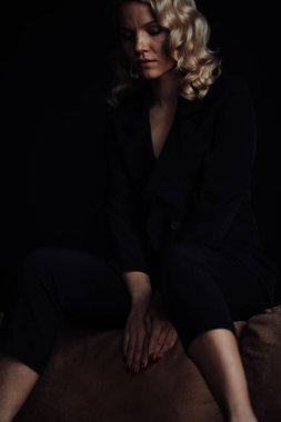 Young adult beauty woman in formal evening suit of black color with lace bra at thoughtful. Stylish blonde curly hair sensual model fashionista posing at studio in fashion pantsuit