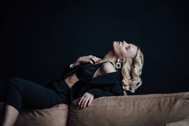 Young adult beauty woman in formal evening suit of black color with lace bra at thoughtful. Stylish blonde curly hair sensual model fashionista posing at studio in fashion pantsuit