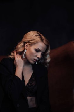 Young adult beauty woman in formal evening suit of black color with lace bra at thoughtful. Stylish blonde curly hair sensual model fashionista posing at studio in fashion pantsuit