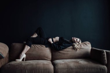 Young adult beauty woman in formal evening suit of black color with lace bra at thoughtful. Stylish blonde curly hair sensual model fashionista posing at studio in fashion pantsuit