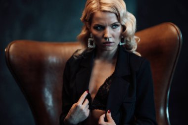 Young adult beauty woman in formal evening suit of black color with lace bra at thoughtful. Stylish blonde curly hair sensual model fashionista posing at studio in fashion pantsuit