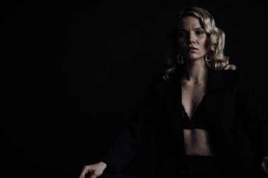 Young adult beauty woman in formal evening suit of black color with lace bra at thoughtful. Stylish blonde curly hair sensual model fashionista posing at studio in fashion pantsuit