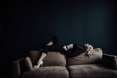 Young adult beauty woman in formal evening suit of black color with lace bra at thoughtful. Stylish blonde curly hair sensual model fashionista posing at studio in fashion pantsuit