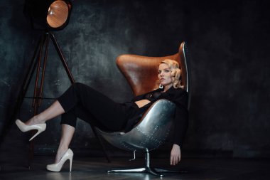 Young adult beauty woman in formal evening suit of black color with lace bra at thoughtful. Stylish blonde curly hair sensual model fashionista posing at studio in fashion pantsuit