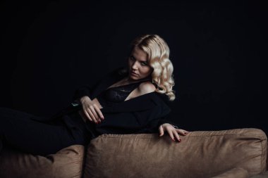 Young adult beauty woman in formal evening suit of black color with lace bra at thoughtful. Stylish blonde curly hair sensual model fashionista posing at studio in fashion pantsuit