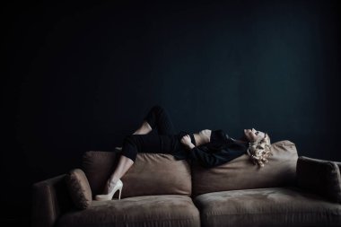 Young adult beauty woman in formal evening suit of black color with lace bra at thoughtful. Stylish blonde curly hair sensual model fashionista posing at studio in fashion pantsuit