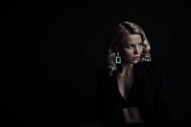 Young adult beauty woman in formal evening suit of black color with lace bra at thoughtful. Stylish blonde curly hair sensual model fashionista posing at studio in fashion pantsuit