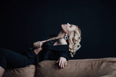 Young adult beauty woman in formal evening suit of black color with lace bra at thoughtful. Stylish blonde curly hair sensual model fashionista posing at studio in fashion pantsuit