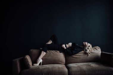 Young adult beauty woman in formal evening suit of black color with lace bra at thoughtful. Stylish blonde curly hair sensual model fashionista posing at studio in fashion pantsuit