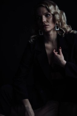 Young adult beauty woman in formal evening suit of black color with lace bra at thoughtful. Stylish blonde curly hair sensual model fashionista posing at studio in fashion pantsuit