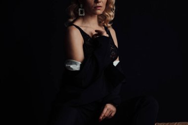 Young adult beauty woman in formal evening suit of black color with lace bra at thoughtful. Stylish blonde curly hair sensual model fashionista posing at studio in fashion pantsuit