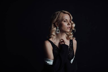 Young adult beauty woman in formal evening suit of black color with lace bra at thoughtful. Stylish blonde curly hair sensual model fashionista posing at studio in fashion pantsuit