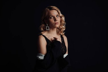 Young adult beauty woman in formal evening suit of black color with lace bra at thoughtful. Stylish blonde curly hair sensual model fashionista posing at studio in fashion pantsuit