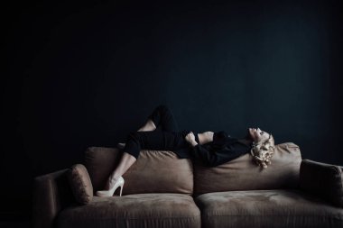 Young adult beauty woman in formal evening suit of black color with lace bra at thoughtful. Stylish blonde curly hair sensual model fashionista posing at studio in fashion pantsuit