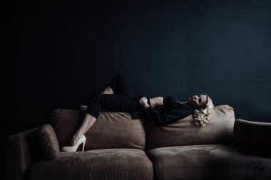 Young adult beauty woman in formal evening suit of black color with lace bra at thoughtful. Stylish blonde curly hair sensual model fashionista posing at studio in fashion pantsuit